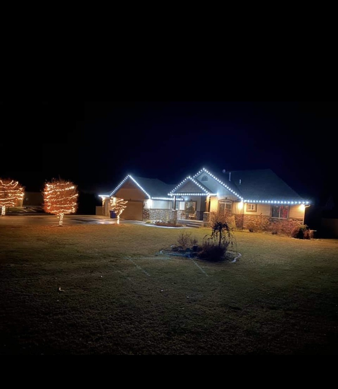 Home in Shelley Idaho with warm white C9 roofline lights and warm white wrapped trees at night