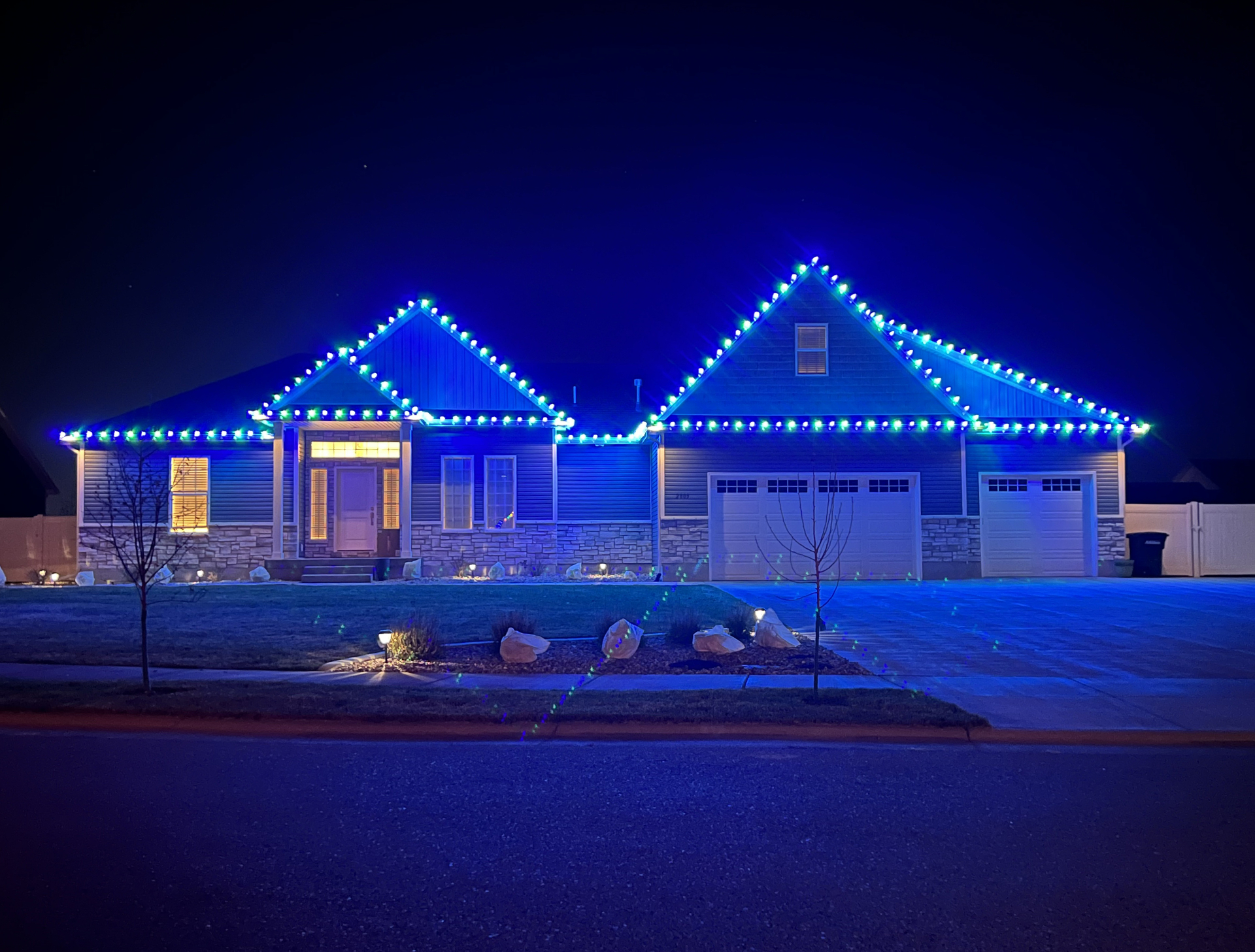 Stone-front home in Idaho Falls with alternating blue and green C9 Christmas lights along the roofline
